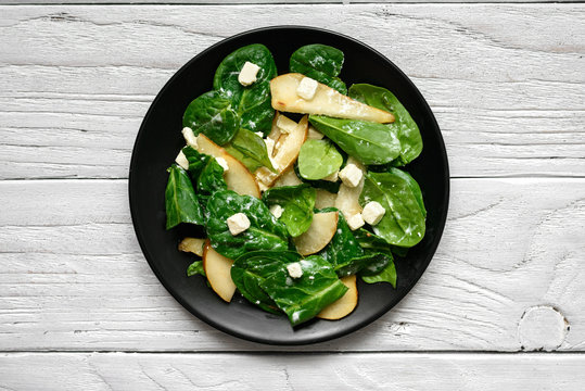 salad with spinach leaves, pear and feta cheese in black plate.