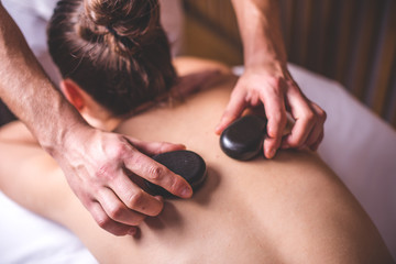 The male hands of the masseur lay hot stones on the girl's shoulder blades. - 189230304