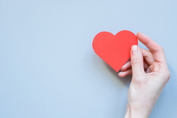 Fototapeta premium Hand holding red paper heart on the blue background. With copy space