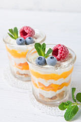 Two portions of homemade dessert cream with peaches, fresh berries and mint in a glass on a light background