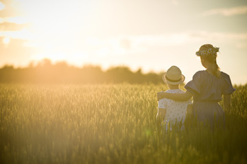 back view on young mother hugging her kid son on the wheat field in the sunset. Happy family watching sunset on a summer day.