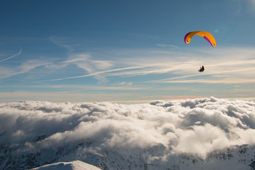 Paragliding above mountain peaks and clouds during winter sunny snowy day