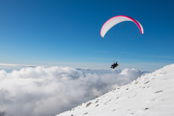 Paragliding above mountain peaks and clouds during winter sunny snowy day