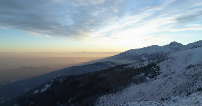 Side aerial top view over winter snowy mountain and woods forest at sunset or sunrise.Blue hour dusk or dawn twilight Alps mountains snow season establisher.4k drone flight establishing shot