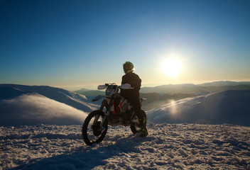 Extreme biker on sport motorcycle on winter snow mountain top on sunset sky
