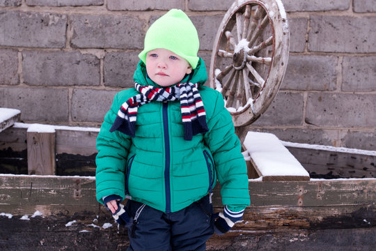 Cute little kid boy in colorful winter clothes playing in rural yard, outdoors during snowfall. Active outdoors leisure with children in winter. Happy child with warm hat, hand gloves