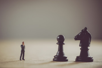 Miniature Businessman in front of chess figures. Business concept