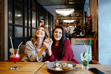 communication and friendship concept - smiling young women with nonalcoholic cocktails at cafe. two girlfriends blonde and brunette talk, joke and laugh
