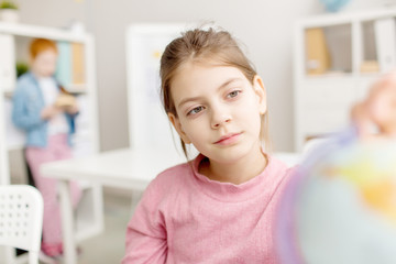 Calm schoolchild looking at globe model at school before lesson of geography