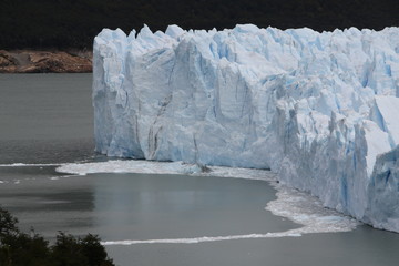 poszarpana struktura argentyńskiego lodowca schodzacego do wody z odłamującymi się bryłami lodu w pochmurny dzień