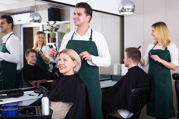 Professional stylist cutting hair of elderly blonde