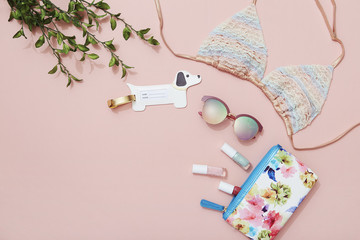 Beach holiday accessories, bikini, sunglasses, makeup bag on pink background, travel flat lay