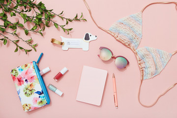 Beach holiday accessories, bikini, sunglasses, makeup bag, notebook on pink background, travel flat lay