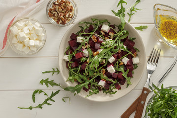 Bowl of beetroot feta salad with arugula and dressing with oil and mustard seeds.