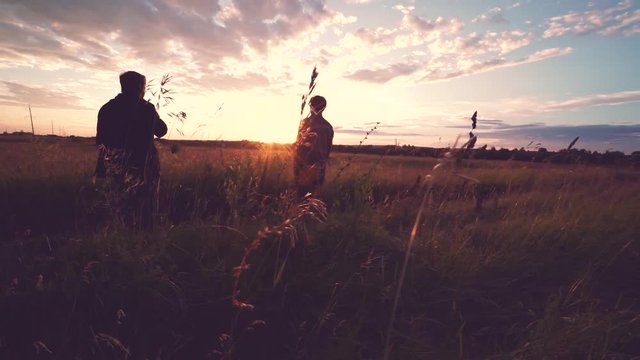 Silhouettes of two young men standing in field at sunset