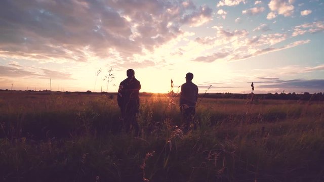 Silhouettes of two young men standing in field at sunset
