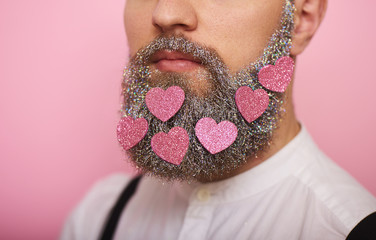 Closeup Portrait of handsome man with pink hearts in beard over pink background