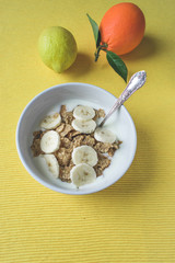 Top view of a bowl of cereals with yogurt and fruits, orange end lemon on bright yellow background. Fitness, healthy diet or breakfast concept 