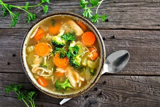 Homemade chicken vegetable soup, top view on an aged rustic wood background