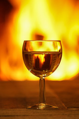 Glass of white wine against cozy fireplace background, winter vacation.