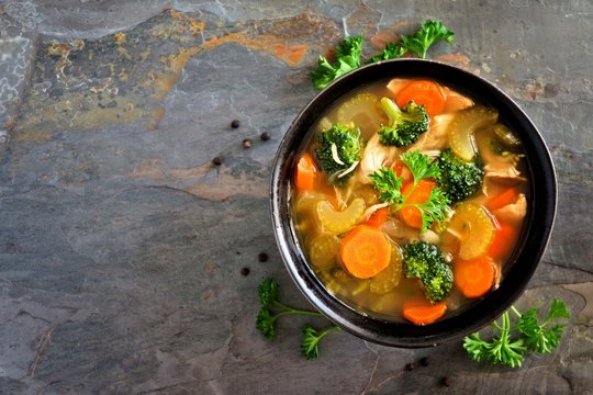 Homemade chicken vegetable soup, overhead view on a dark slate background
