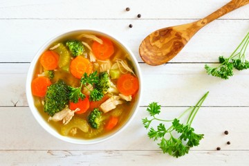 Homemade chicken vegetable soup, above scene on a white wood background