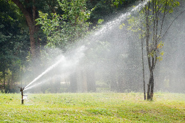 Giant sprinkle watering grass field and trees in the garden