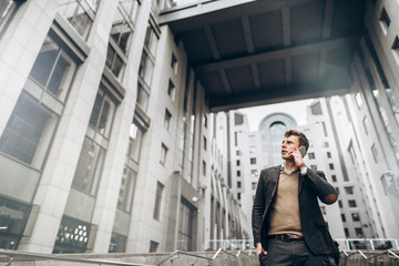 Young attractive businessman in stylish suit which talks on the phone outdoors near business center