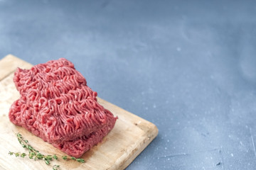 Fresh beef meat in forcemeat, on a wooden board. On a gray stone background. Free space for writing...