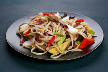 Udon wok noodles with pork and peppers, served on black plate, close up. Japanese cuisine, restaurant concept