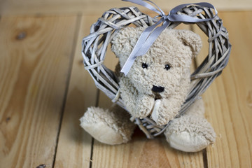 Teddy bear and wicker heart on wooden background. Valentine's Day.