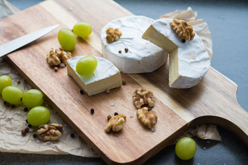 cheese camembert on a wooden board, decoration with nuts and grapes