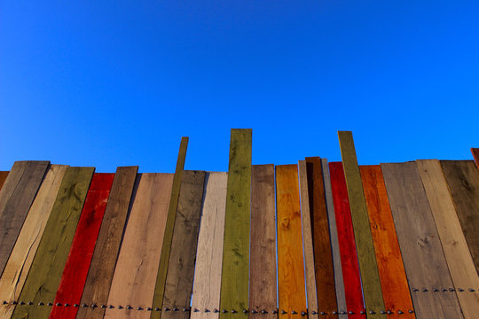 Multicolored wooden wall and blue sky. A colored wall of wood with a lot of copy space. Wooden fence and blue sky. Colored Painted Old Shabby Wooden Desk Background. Wooden Background. © diesel_80