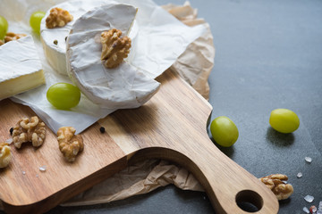 cheese camembert on a wooden board, decoration with nuts and grapes