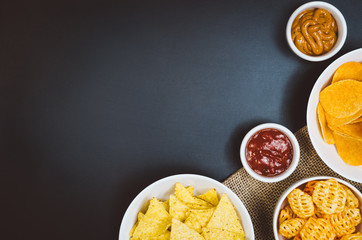 Party snacks - potato chips and snacks in bowl on black slate table. Photograph taken from above, top view with copy space around products.