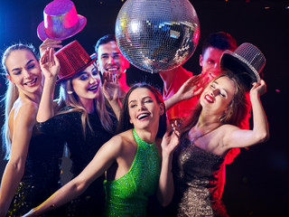 Dance party with group people dancing. Women and men have fun in night club. Happy girl on foreground and disco ball on background. Guys took off their hats. Rest after hard day at work.