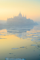 Fototapeta premium Parliament building reflected in Danube river covered with floe in yellow haze, Budapest