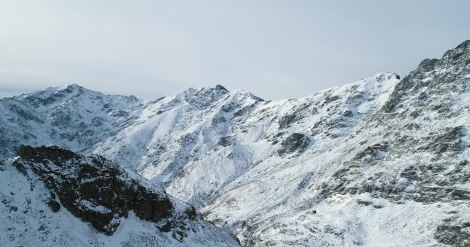 Forward aerial top view over winter snowy mountain rock peaks.Rocky mountains summits covered in snow and ice glacier.Winter wild nature scape outdoor establisher.4k drone flight establishing shot