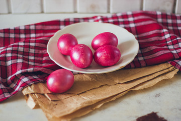 Bright red Easter eggs on the white plate on the checked red towel and craft brown paper on the table