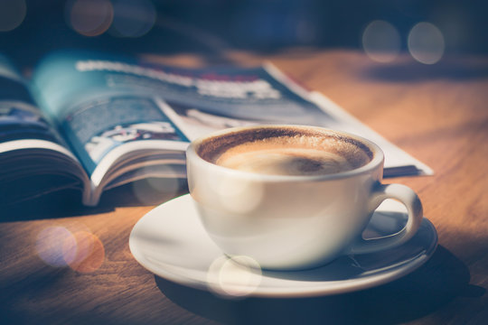 cup of coffee with magazine on table in cafe in dark tone and vintage .