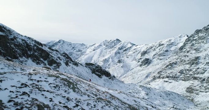 Side aerial over winter snowy mountain pass with mountaineering skier people walking up climbing.snow covered mountains top and ice glacier.Winter wild nature outdoor establisher.4k drone flight