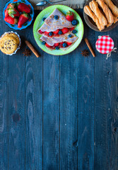 Fresh homemade crepes served on a plate with strawberries and blueberries, on a dark wooden background,