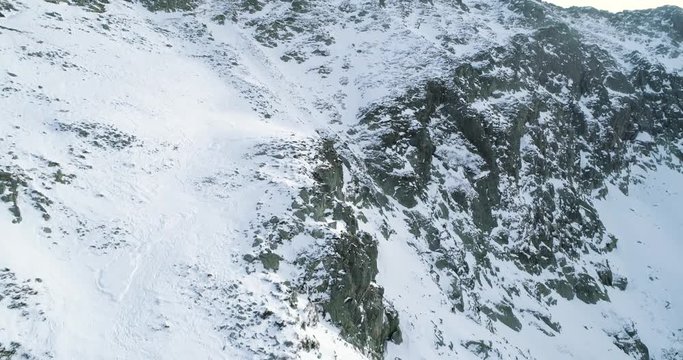 Backward discover aerial over winter snowy mountain with mountaineering skier people walking up climbing.snow covered mountains top ice glacier.Winter wild nature outdoor establisher.4k drone flight
