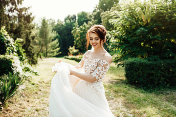 bride in a dress standing in a green garden and holding a wedding bouquet of flowers and greenery