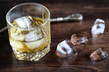 Whiskey in a glass and pieces of ice on a wood