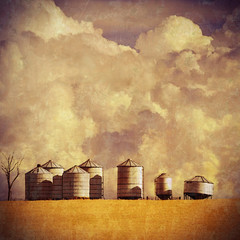 Grunge vintage textured farm silos and wheat field with cloud-filled sky background illustration