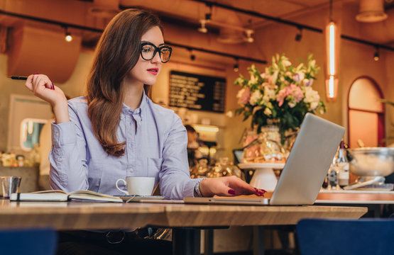 Young businesswoman is sitting in cafe at table, working on laptop. Hipster girl blogging, browsing internet, learning online, checking email.Online marketing,education, e-learning.Freelance, startup.