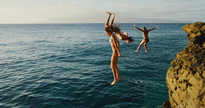 Friends cliff jumping into the ocean at sunset