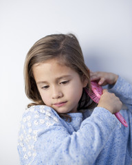 Young girl with far off look while brushing hair with pink brush