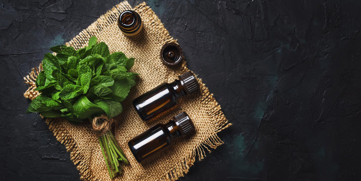 Essential oil of peppermint in a small brown bottle with fresh green mint, black background, top view